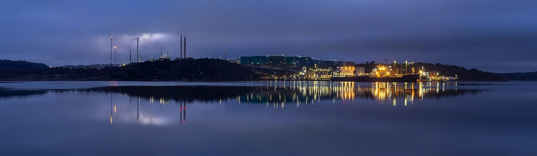 A fuel terminal at blue hour, its lights reflected on still water